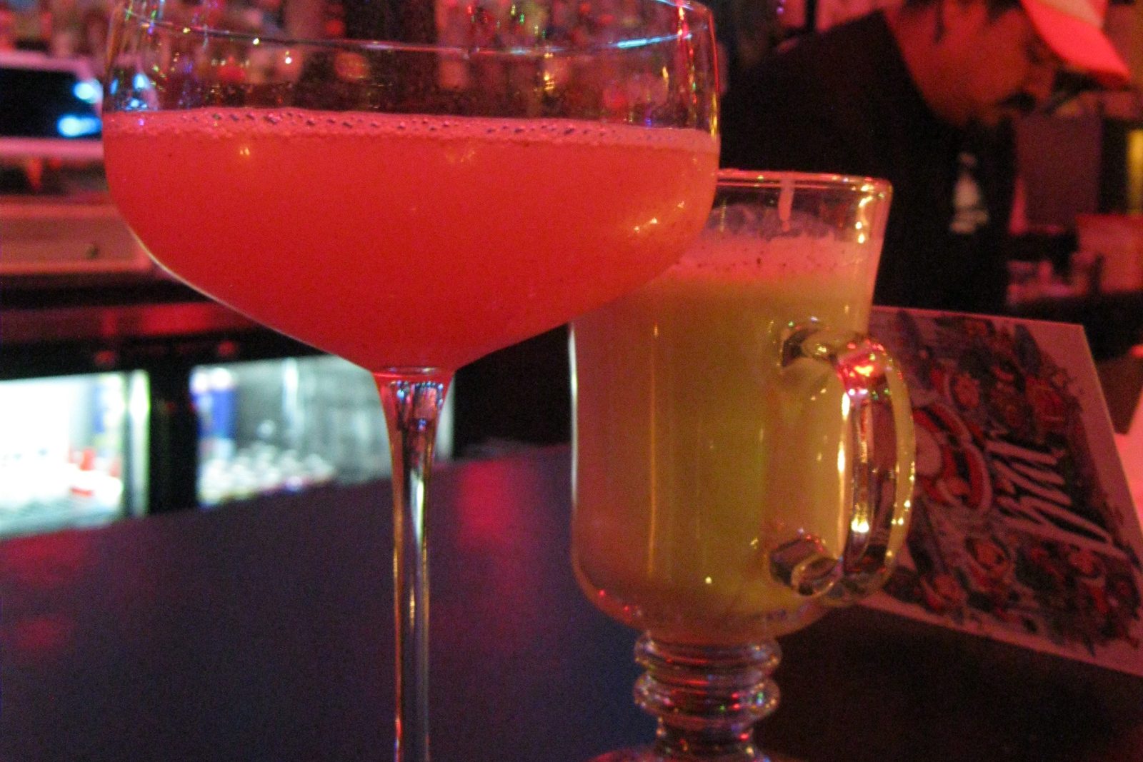 Two cocktails on a bar under neon nightlife lights
