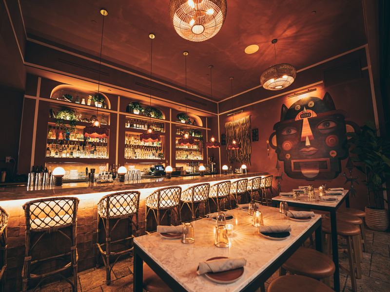 Dining room at Mírate in Los Feliz with a lit back bar and marble-topped tables